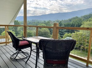 Enjoy a serene view of the surrounding mountains from this deck with a table and two chairs.