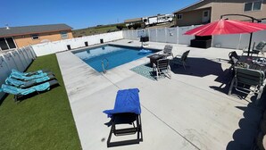 En trädgård med en pool, solstolar och en täckt uteplats.