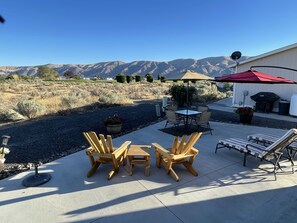 Une terrasse avec des chaises et une table en bois, un parasol rouge et une vue sur les montagnes.
