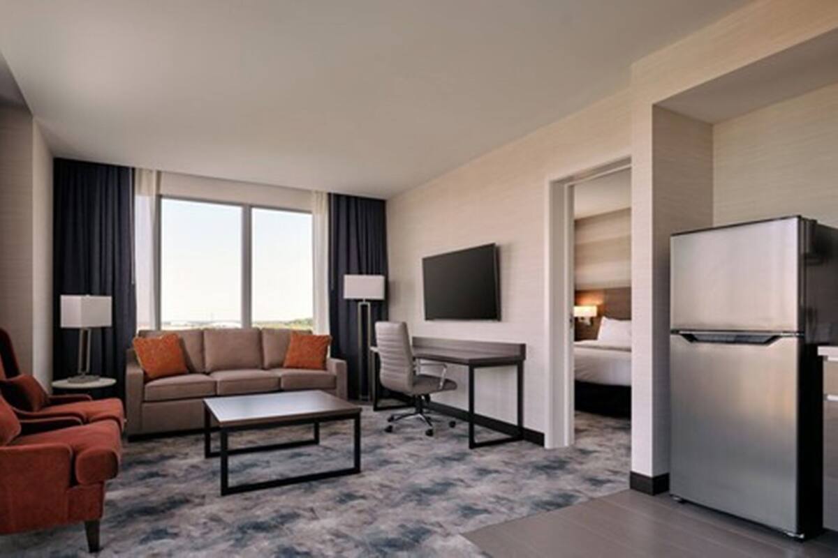 Habitación de hotel con sofá, sillón, escritorio y refrigerador.