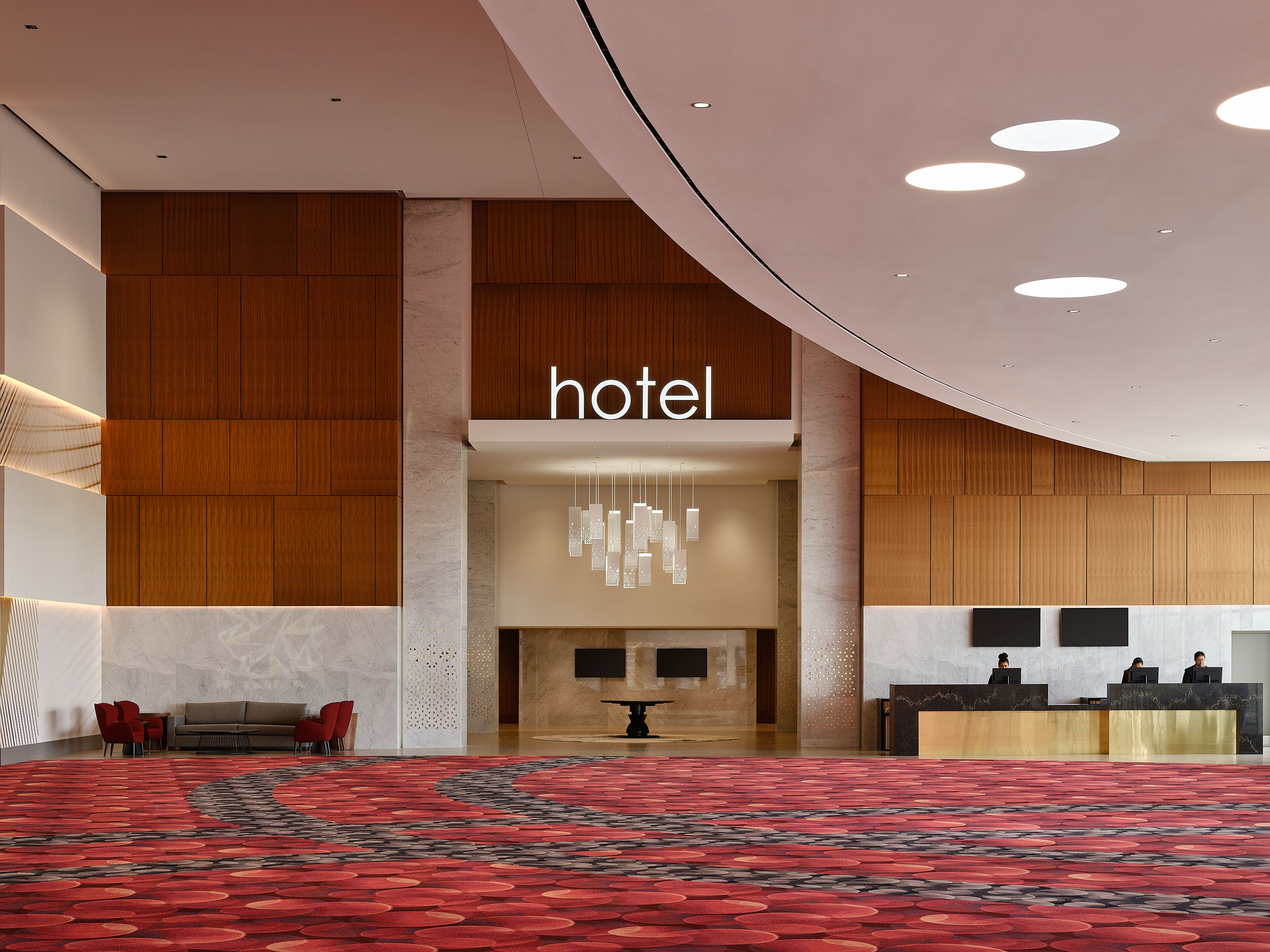 Eine Hotelhalle mit Empfangstresen, Sitzgelegenheiten und einem großen, rot gemusterten Teppich.