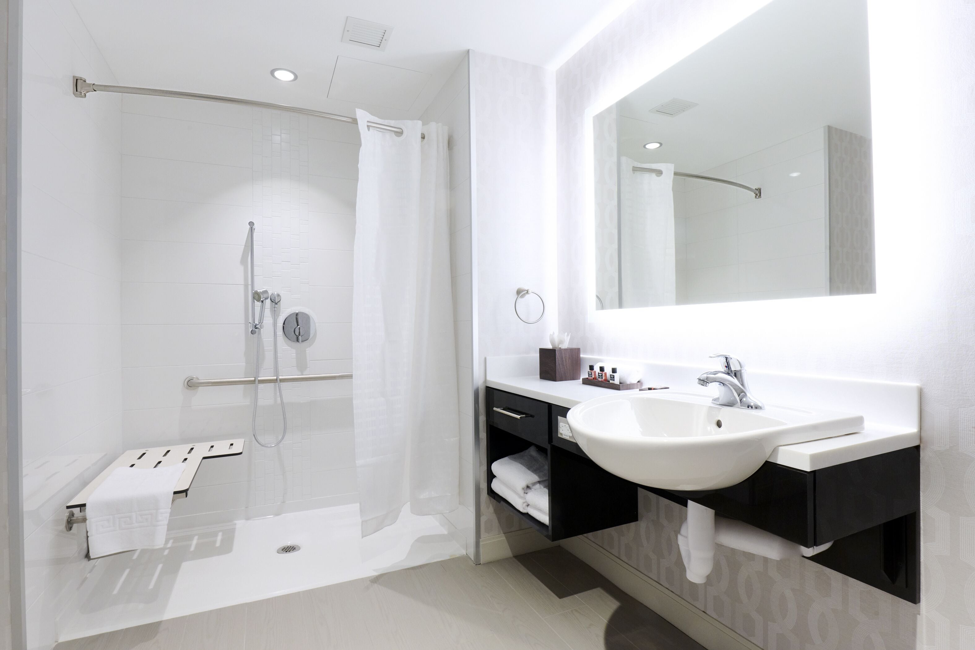 Un baño moderno con ducha de vidrio, un espejo grande y un lavabo blanco.