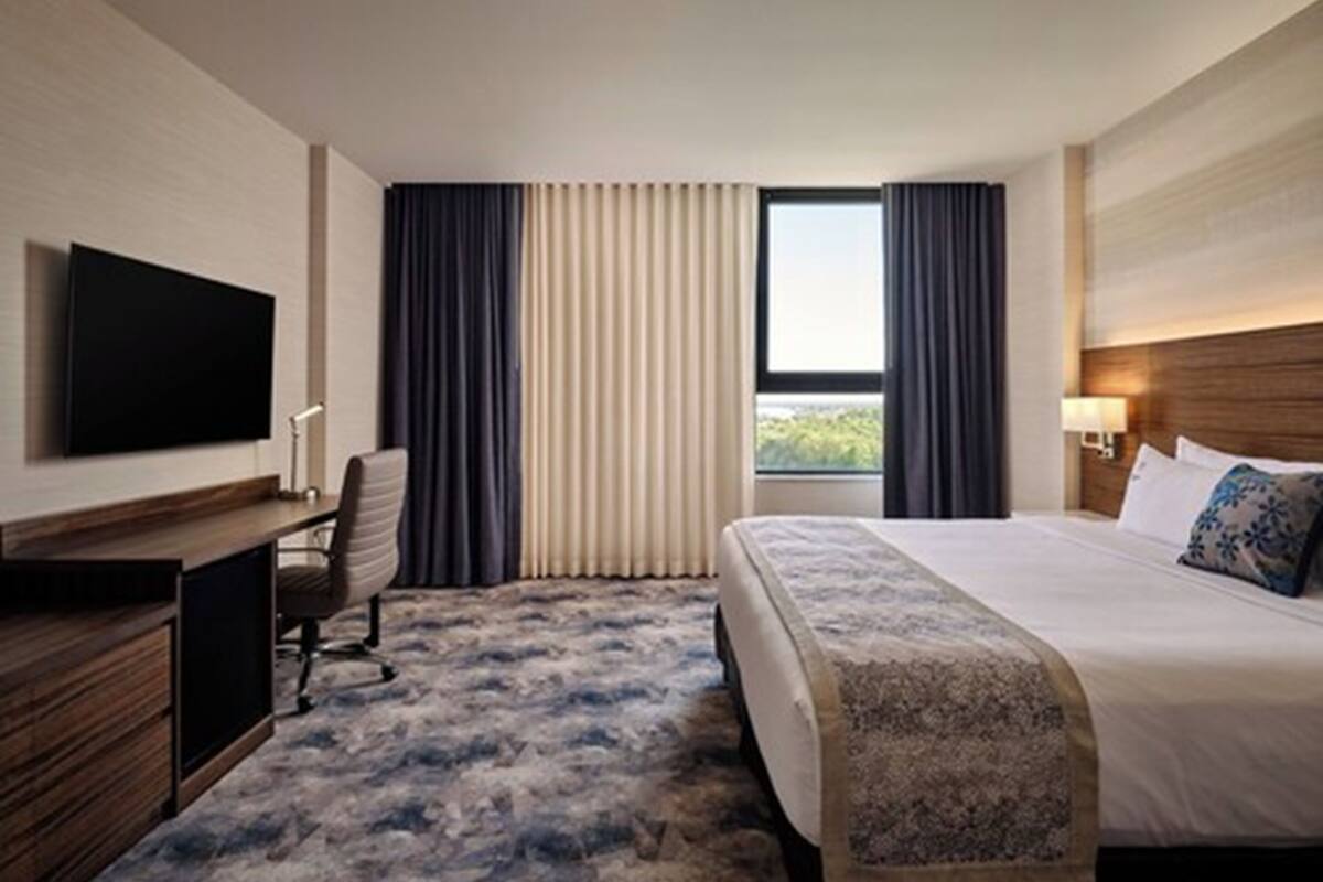 Una habitación de hotel con cama, un escritorio con silla, televisión y ventana con cortinas.
