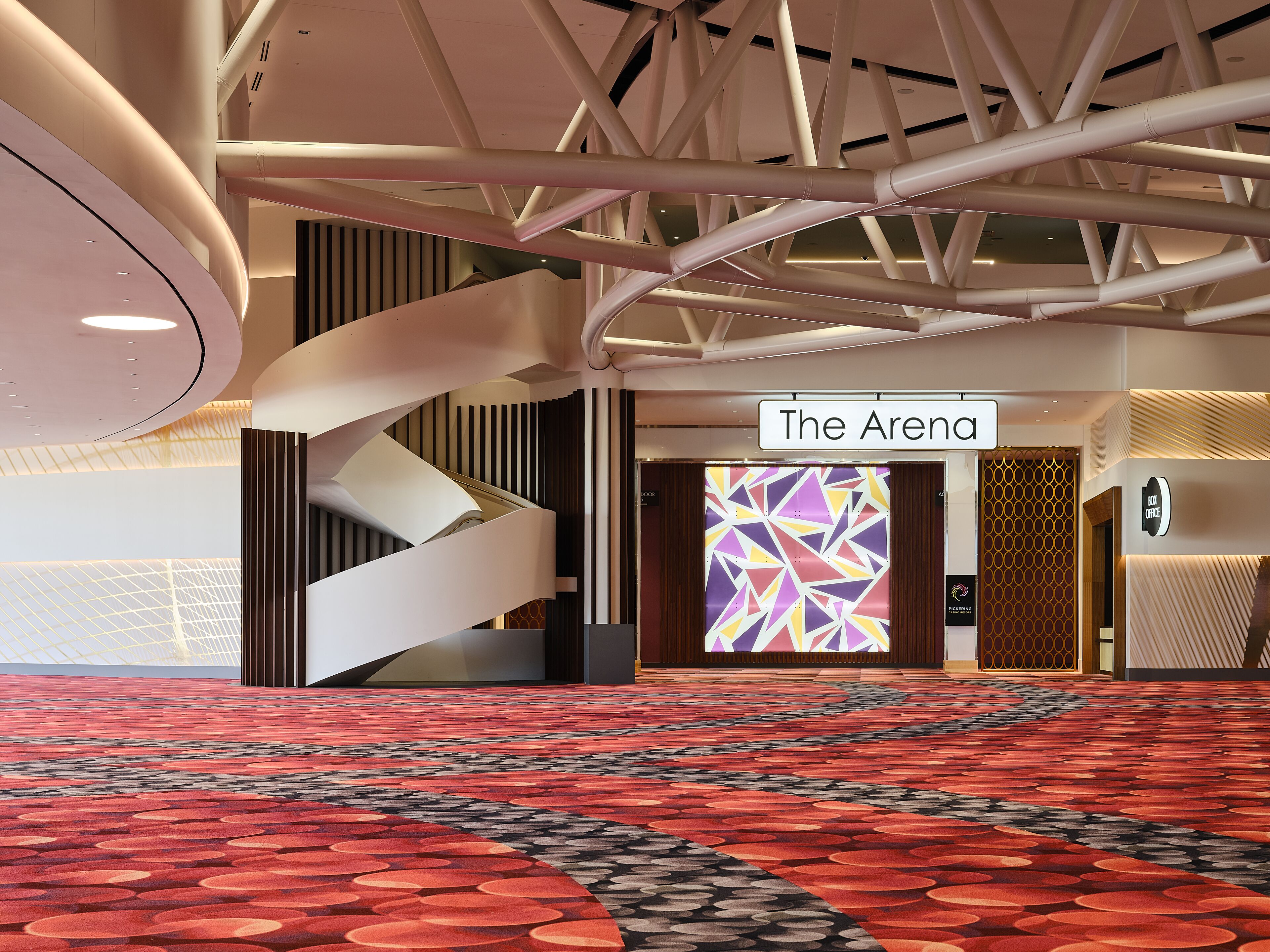 A modern hotel lobby with a red carpet, a sign reading "The Arena," and a geometric patterned wall.