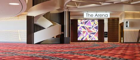 Un moderno hall de hotel con alfombra roja, un cartel que dice "The Arena" y una pared con estampado geométrico.