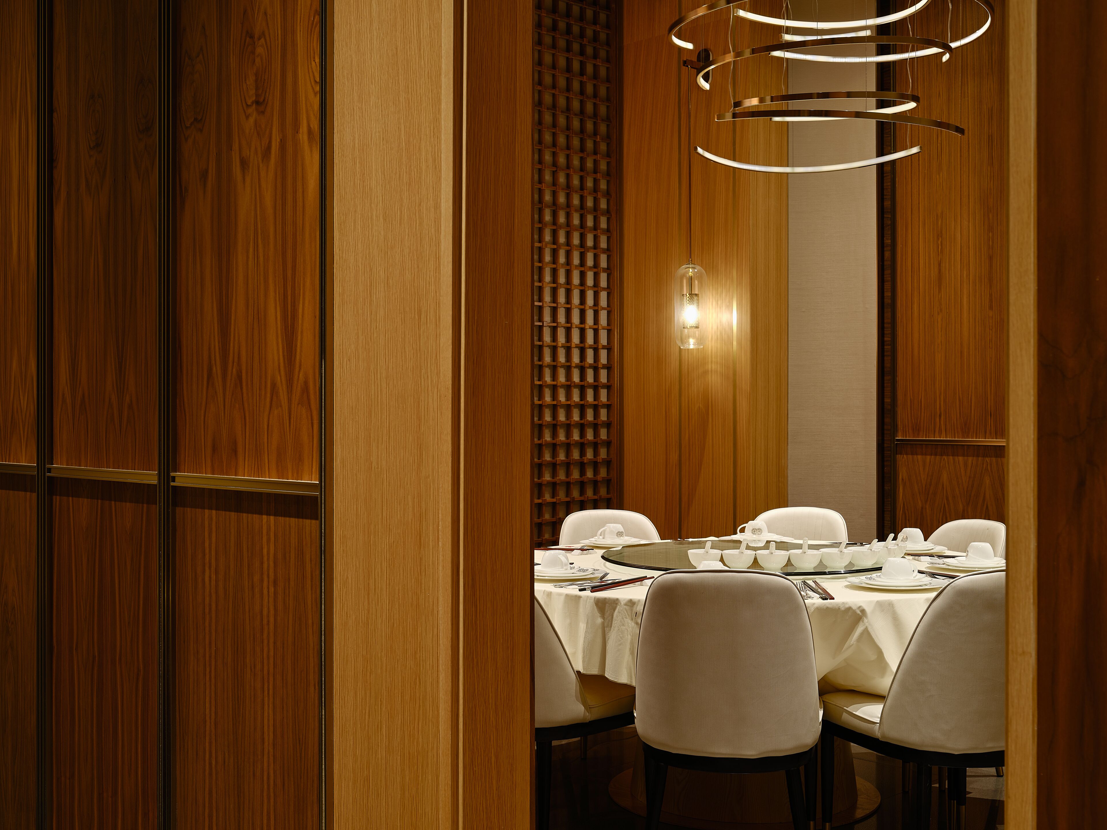 Un comedor con un panel de madera, una lámpara colgante moderna y una mesa dispuesta para cuatro.