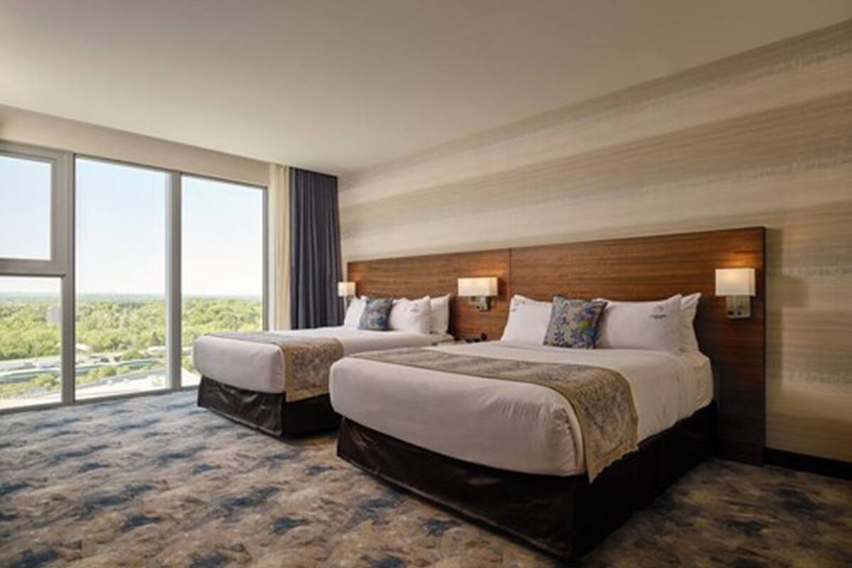 Habitación de hotel con dos camas, ventanas amplias y vistas al paisaje.