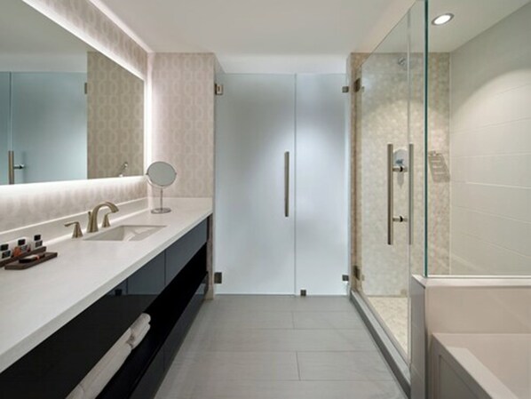A modern bathroom with a large mirror, two sinks, a glass-enclosed shower, and a dark-colored vanity.
