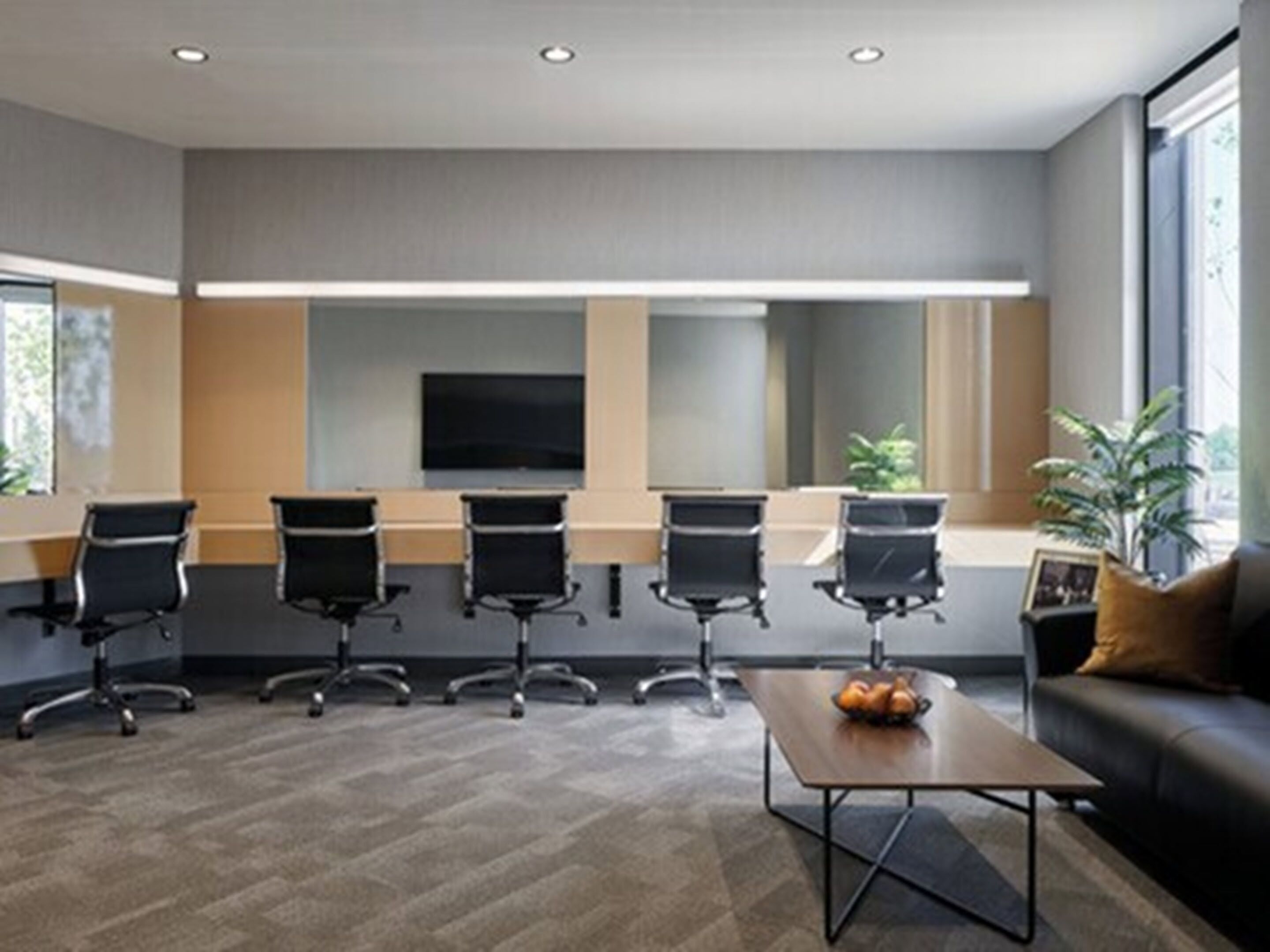 A conference room with a large screen, four black chairs, a coffee table, and a sofa with a plant.