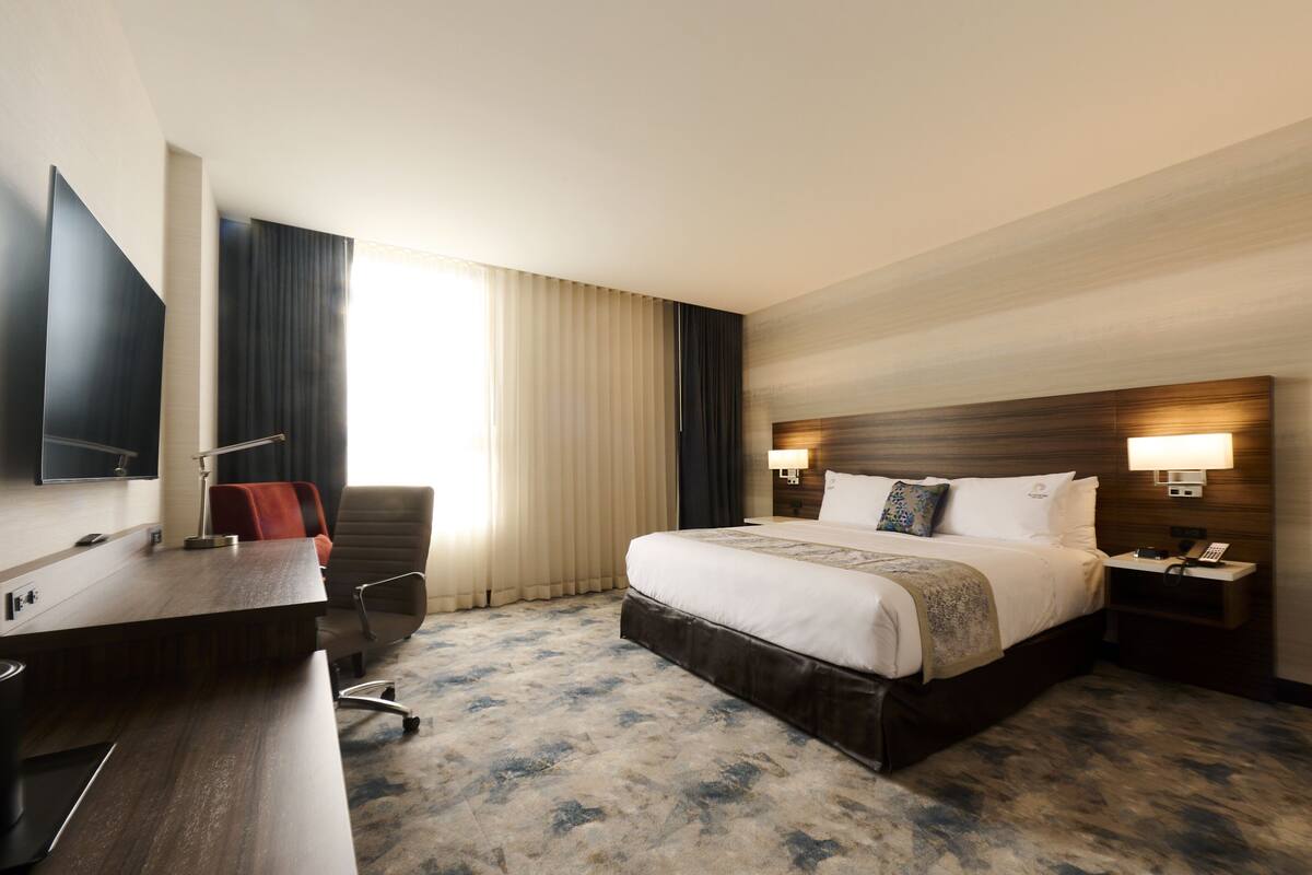 Habitación de hotel con una cama grande, un escritorio, una silla, un televisor y una ventana con cortinas.