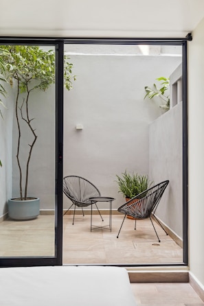 Un patio moderno con dos sillas, una planta en maceta y una pequeña mesa.