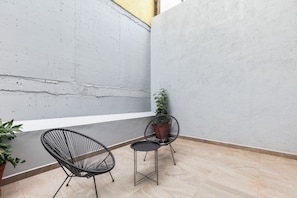 Un petit espace extérieur aménagé avec deux chaises et une table, un pot de fleurs et un mur en béton.