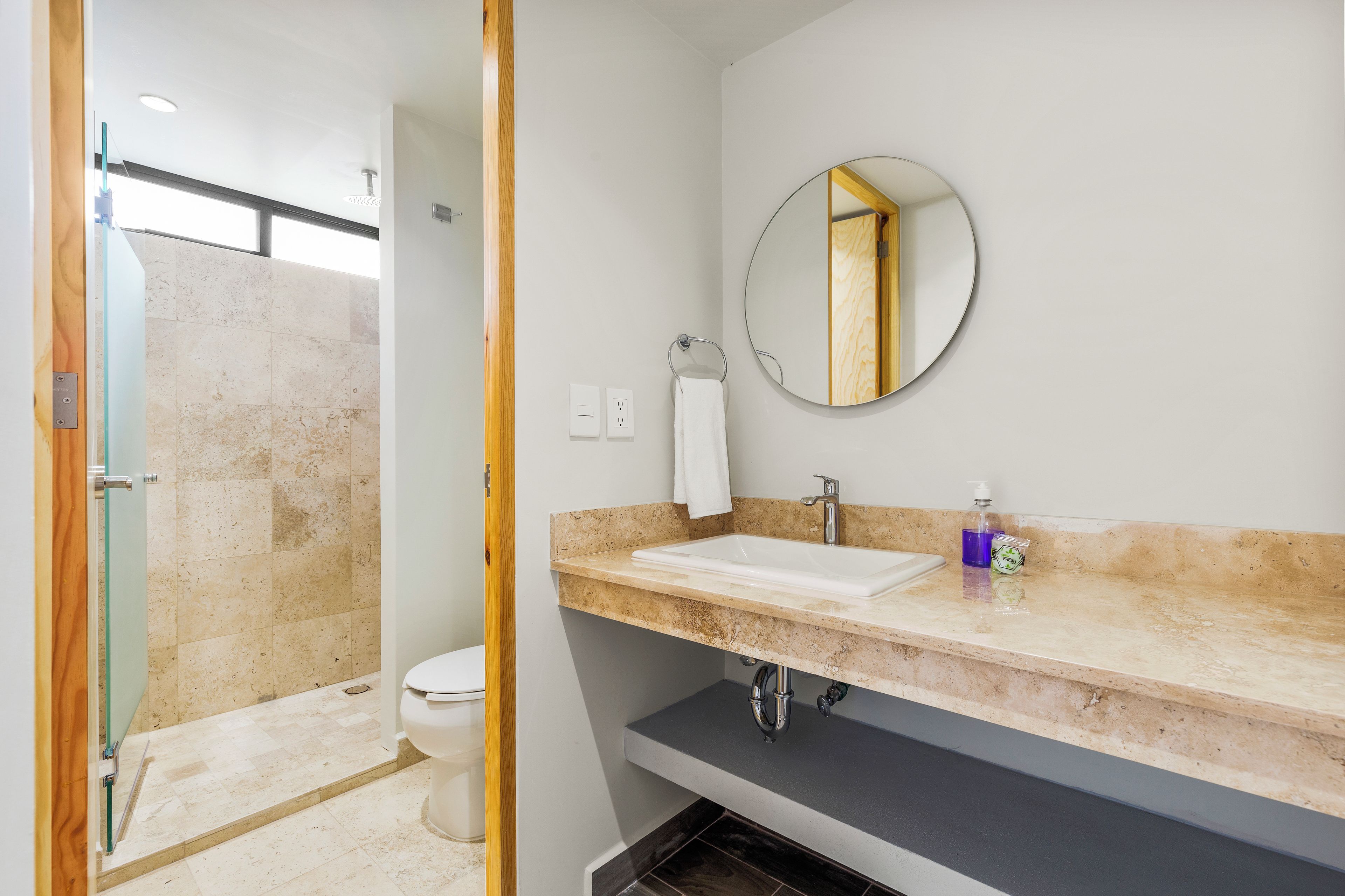 A bathroom with a shower, toilet, sink, and a mirror.