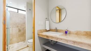 A bathroom with a shower, toilet, sink, and a mirror.