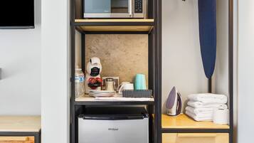 A compact kitchenette with a built-in microwave, a refrigerator, and a small ironing board.