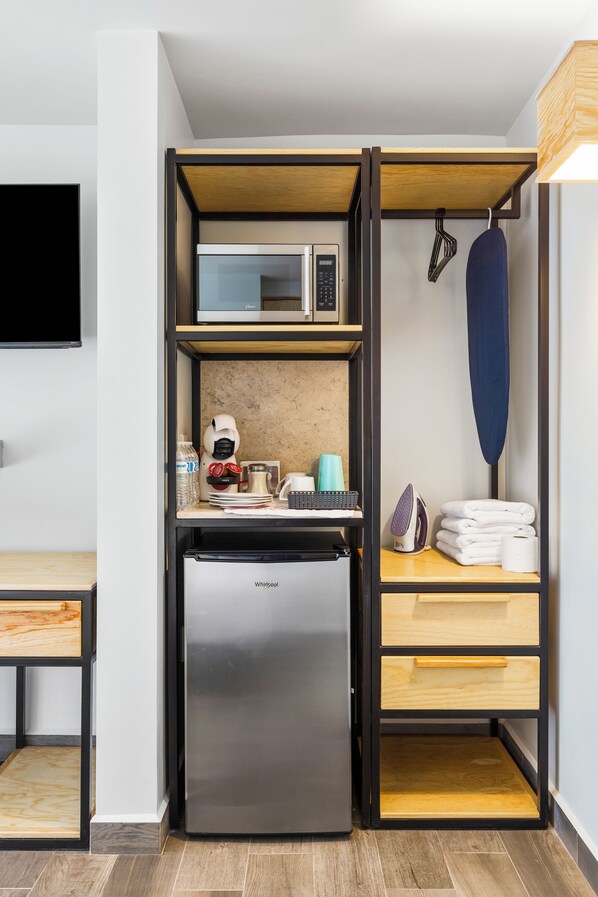 Una kitchenette compacta con microondas integrado, refrigerador y una plancha pequeña.