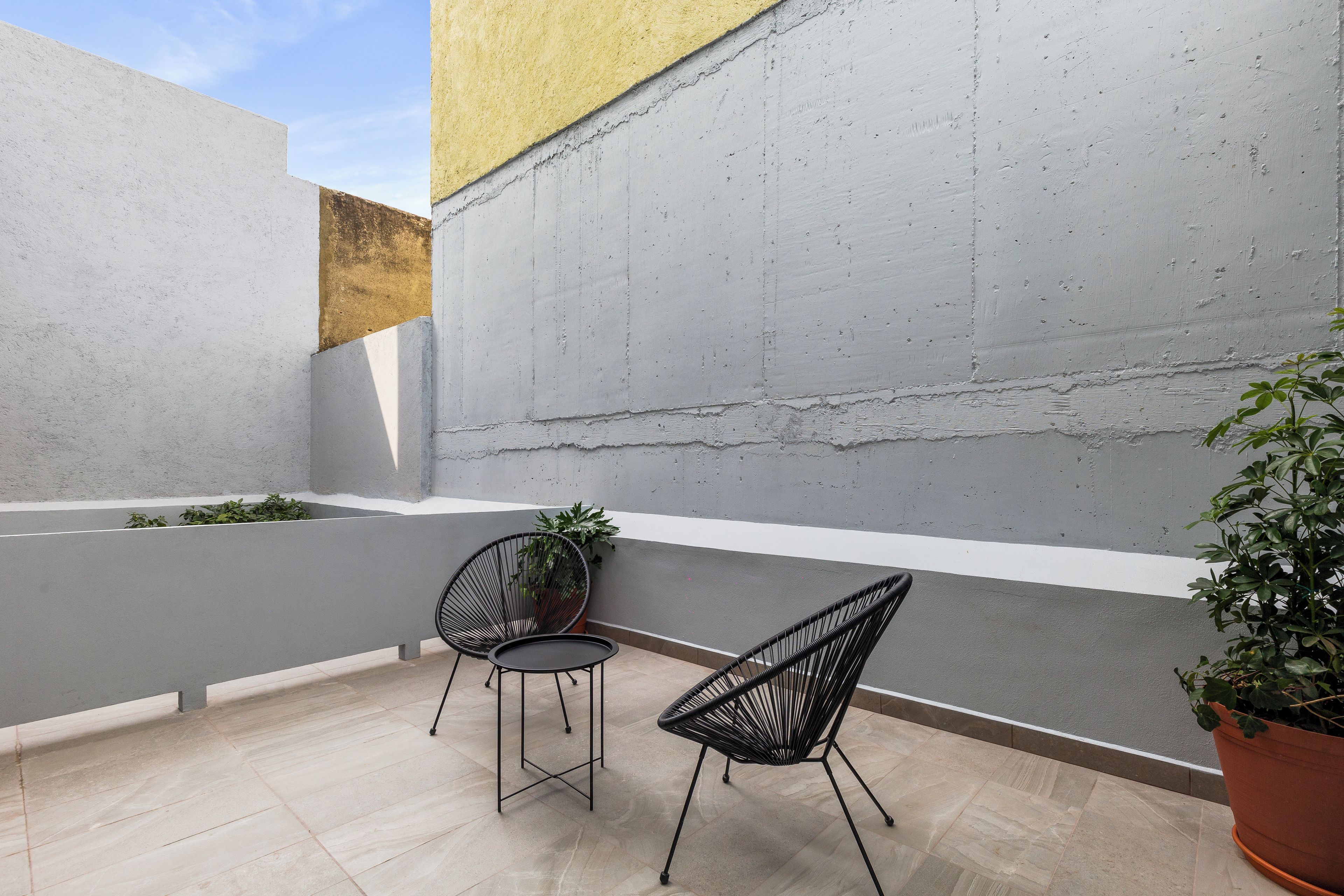 A small outdoor seating area with two chairs and a table, a potted plant, and a concrete wall.