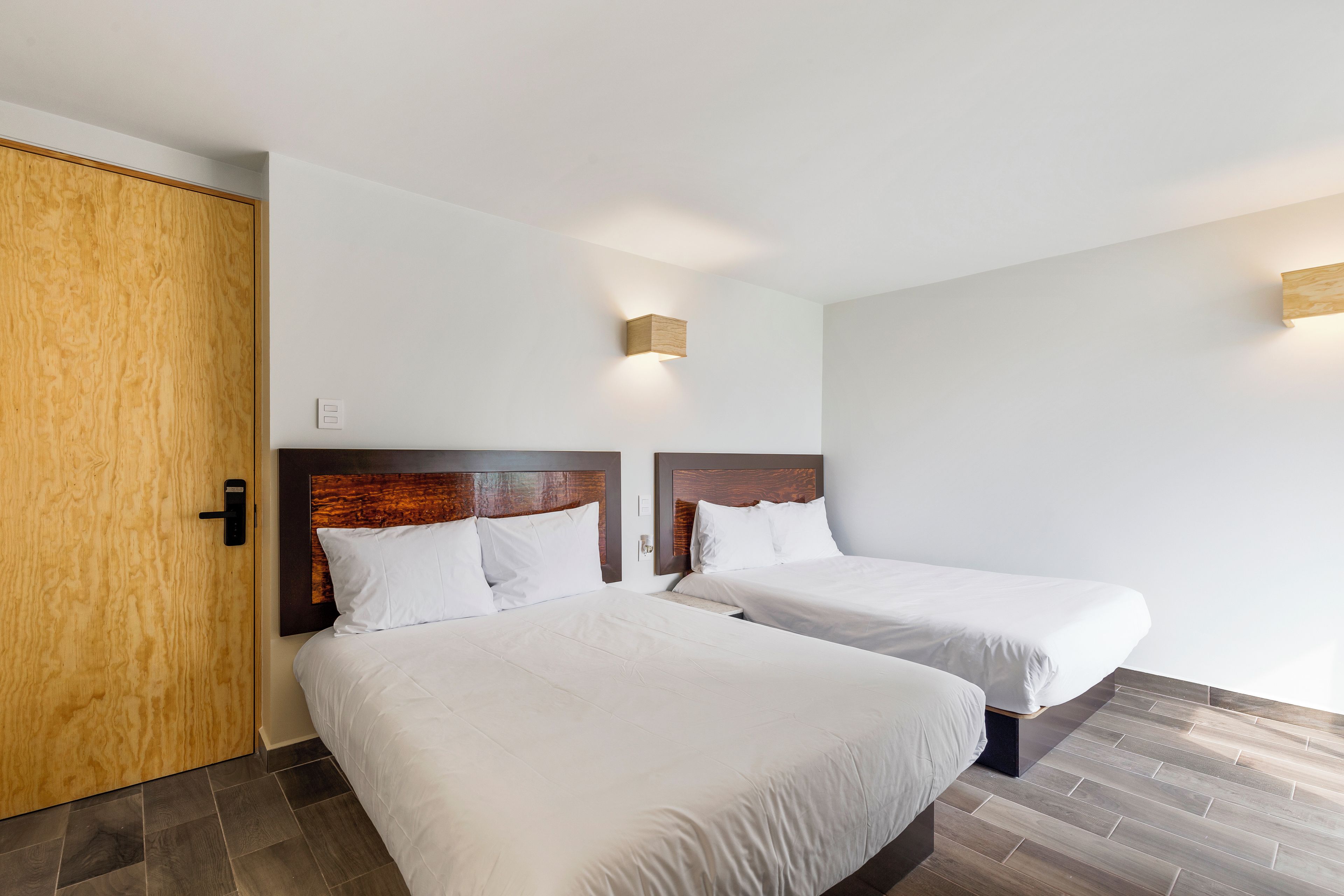 A hotel room with two beds, a wooden door, and a wall-mounted light fixture.