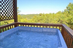 Relax in a hot tub on a spacious deck surrounded by lush greenery.