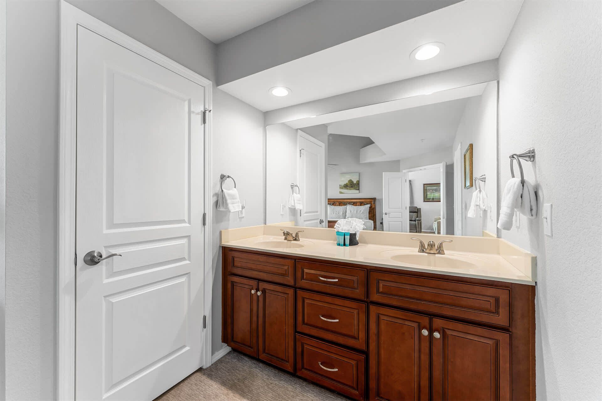 A bathroom with a double vanity, wooden cabinets, a large mirror, and a door.