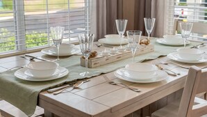 Mesa de comedor lista para seis personas, con platos, vasos y cubiertos.