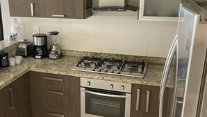 A kitchen with a gas stove, oven, coffee maker, and a refrigerator. - Condominios AR (Puerto Vallarta)