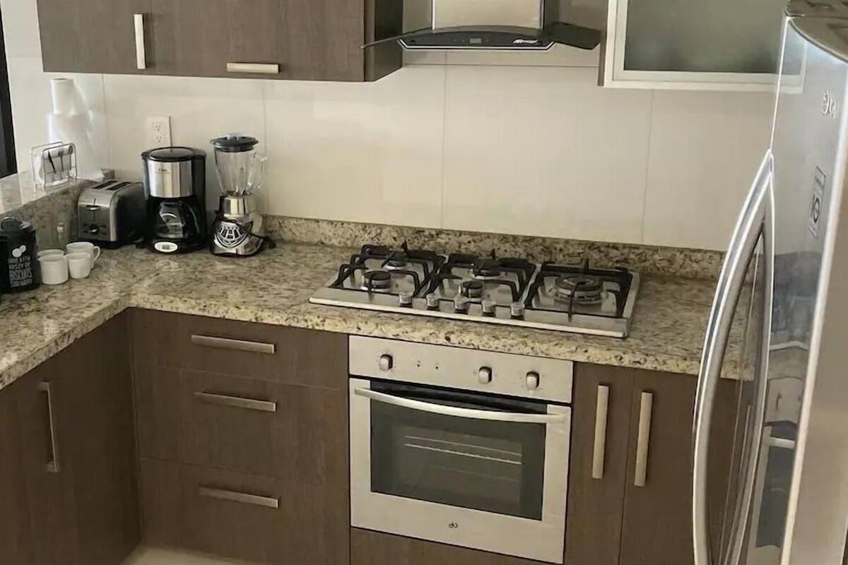 Una cocina equipada con estufa a gas, horno, cafetera y refrigerador.