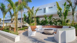 A modern outdoor lounge area with a circular seating arrangement, a fire pit, and lush greenery including palm trees. - Condominios AR (Puerto Vallarta)