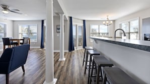A modern kitchen with a bar area, wooden flooring, and large windows. - "Siren's Song" Oceanfront Beach House w/pool (Murrells Inlet)