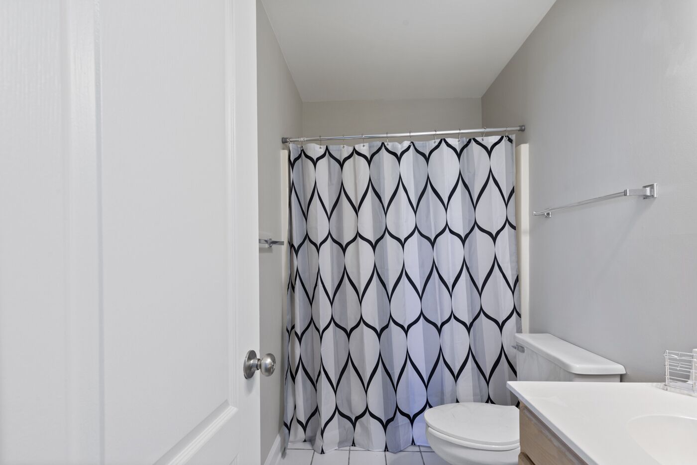 Un baño con inodoro y lavamanos blancos, y cortina de ducha con estampado geométrico.