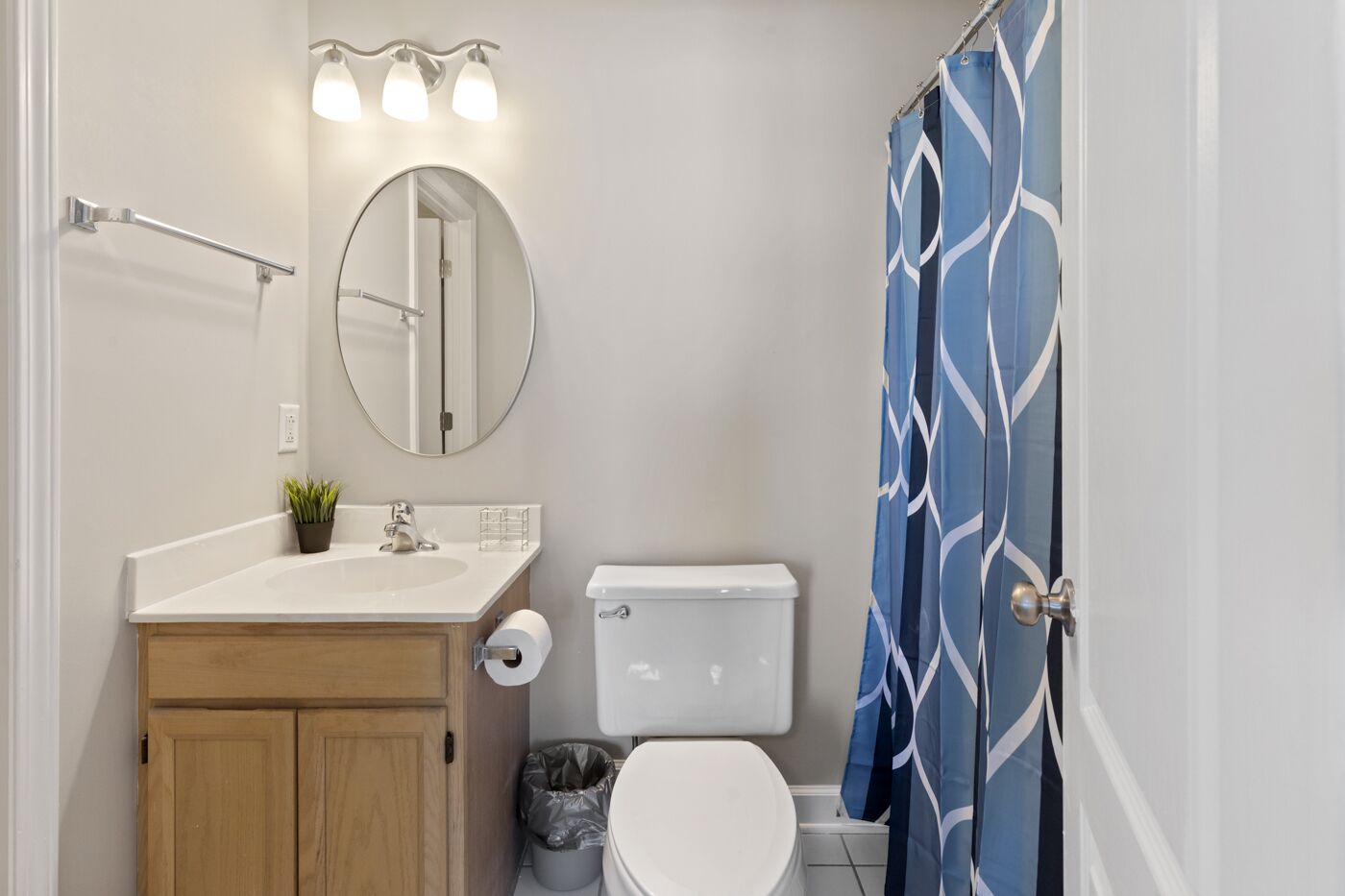 Une salle de bain avec un lavabo blanc, un miroir et des toilettes, un meuble en bois et un rideau de douche bleu à motifs.