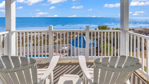 A covered outdoor area with white chairs facing a pool and a view of the ocean. - "Siren's Song" Oceanfront Beach House w/pool (Murrells Inlet)