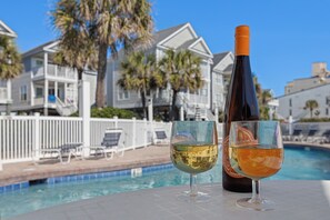 A poolside setting with a bottle and two glasses of wine, a white fence, and houses in the background. - Oceanfront Home, Pool Steps Away, Dogs OK (Murrells Inlet)