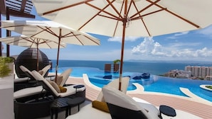 A poolside area with lounge chairs and umbrellas, overlooking a infinity pool and ocean view. - Condominios 180PR (Puerto Vallarta)
