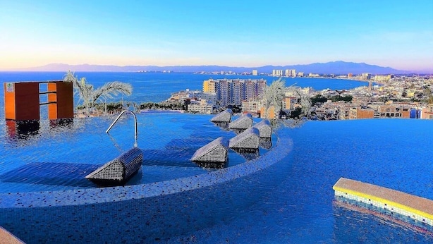 An infinity pool with a city view, a palm tree, and a lifeguard stand. - Condominios 180PR (Puerto Vallarta)