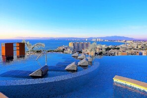 An infinity pool with a city view, a palm tree, and a lifeguard stand. - Condominios 180PR (Puerto Vallarta)