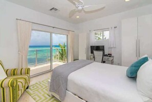 A bedroom with a bed, a TV, a desk, and a view of the ocean. - Ocean's Edge: North Side Grand Cayman Beachfront Villa (North Side)