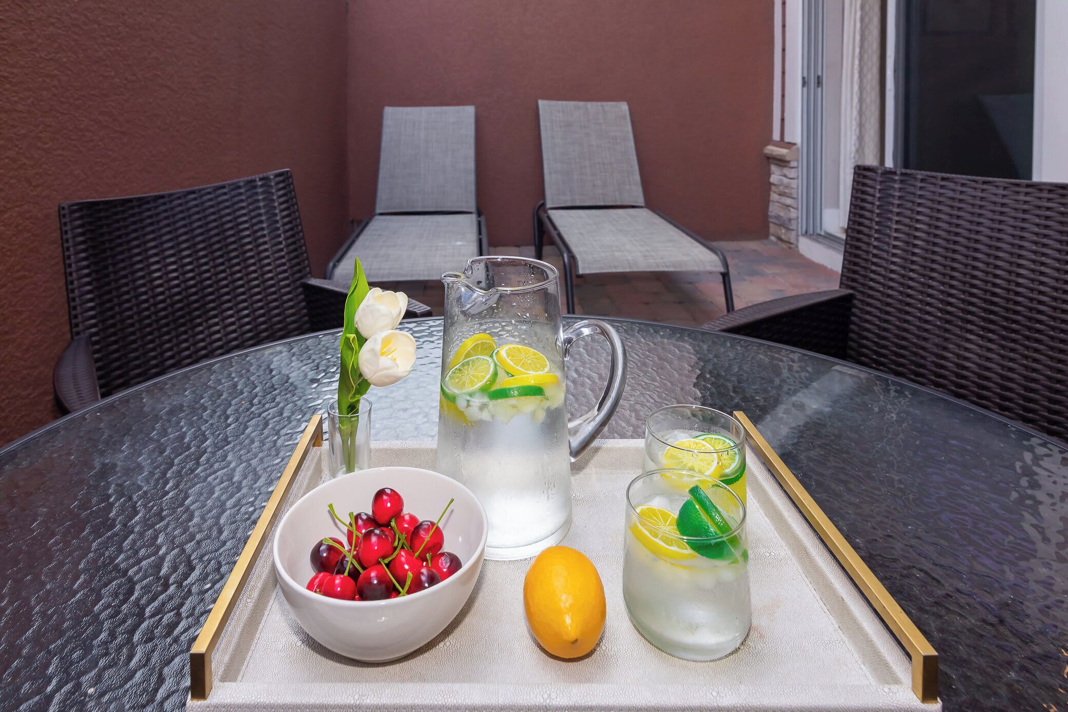 A table with a pitcher of iced tea, a bowl of cherries, and a lemon on a tray.