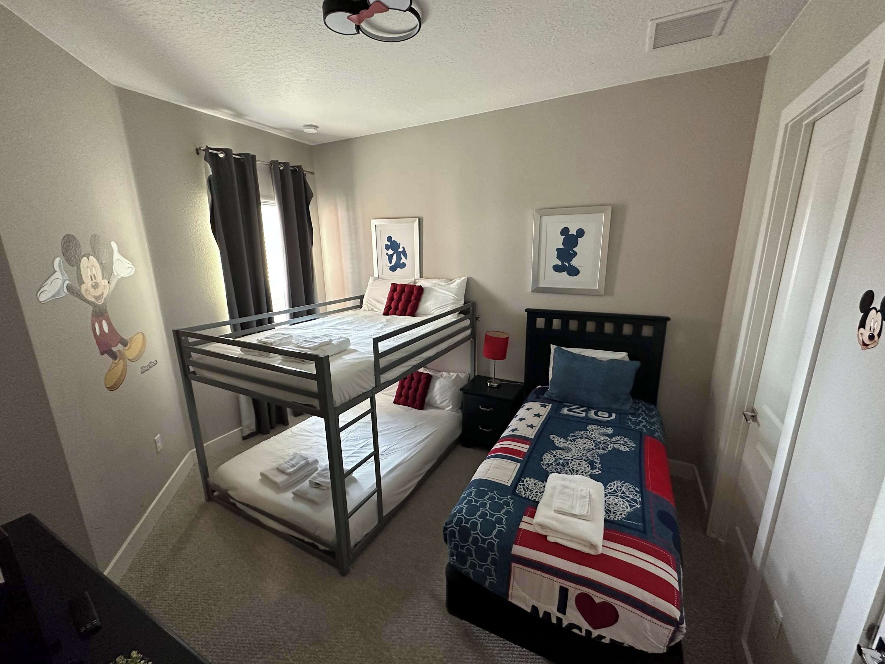 A room with bunk beds, a desk, and a bed with a Mickey Mouse themed blanket.