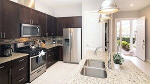 Una cocina moderna con armarios de madera oscura, electrodomésticos de acero inoxidable, encimeras de granito y una lámpara colgante.