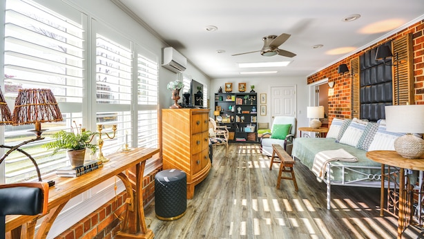 A spacious living room with a large window, a ceiling fan, and a brick accent wall. - 4 Mi to Dtwn: Spacious Suite in Mount Airy (Mt Airy)