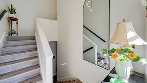 A staircase with wooden steps, a white wall, a mirror, a lamp, and a vase with flowers. - 4 Mi to Dtwn: Spacious Suite in Mount Airy (Mt Airy)