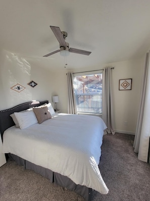 Une chambre à coucher comprenant un lit, un ventilateur de plafond, une fenêtre avec des stores et des éléments de décoration murale.