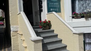 A hotel entrance with a signboard, a staircase, and flower boxes.