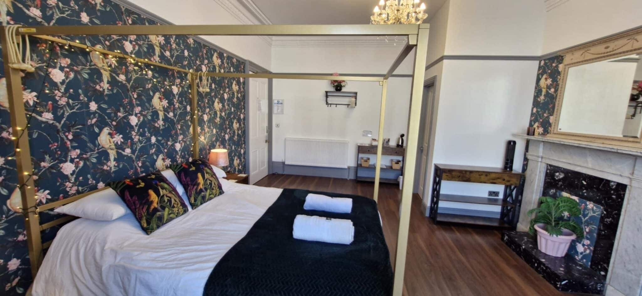 A four-poster bed with floral wallpaper, a fireplace, and a mirror.