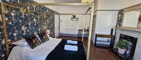 A four-poster bed with floral wallpaper, a fireplace, and a mirror.