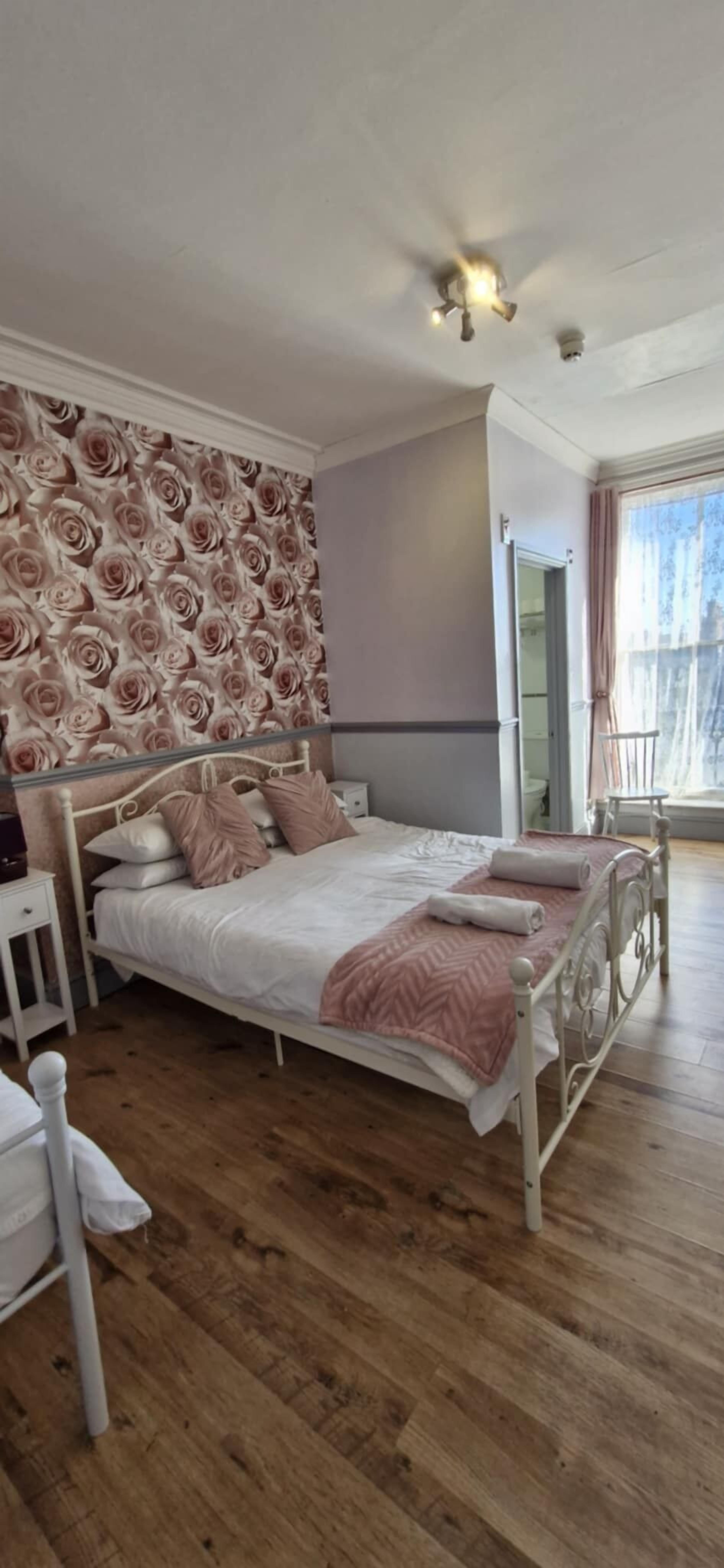 Un dormitorio con cama, mesitas de noche, un espejo y una ventana con cortinas.