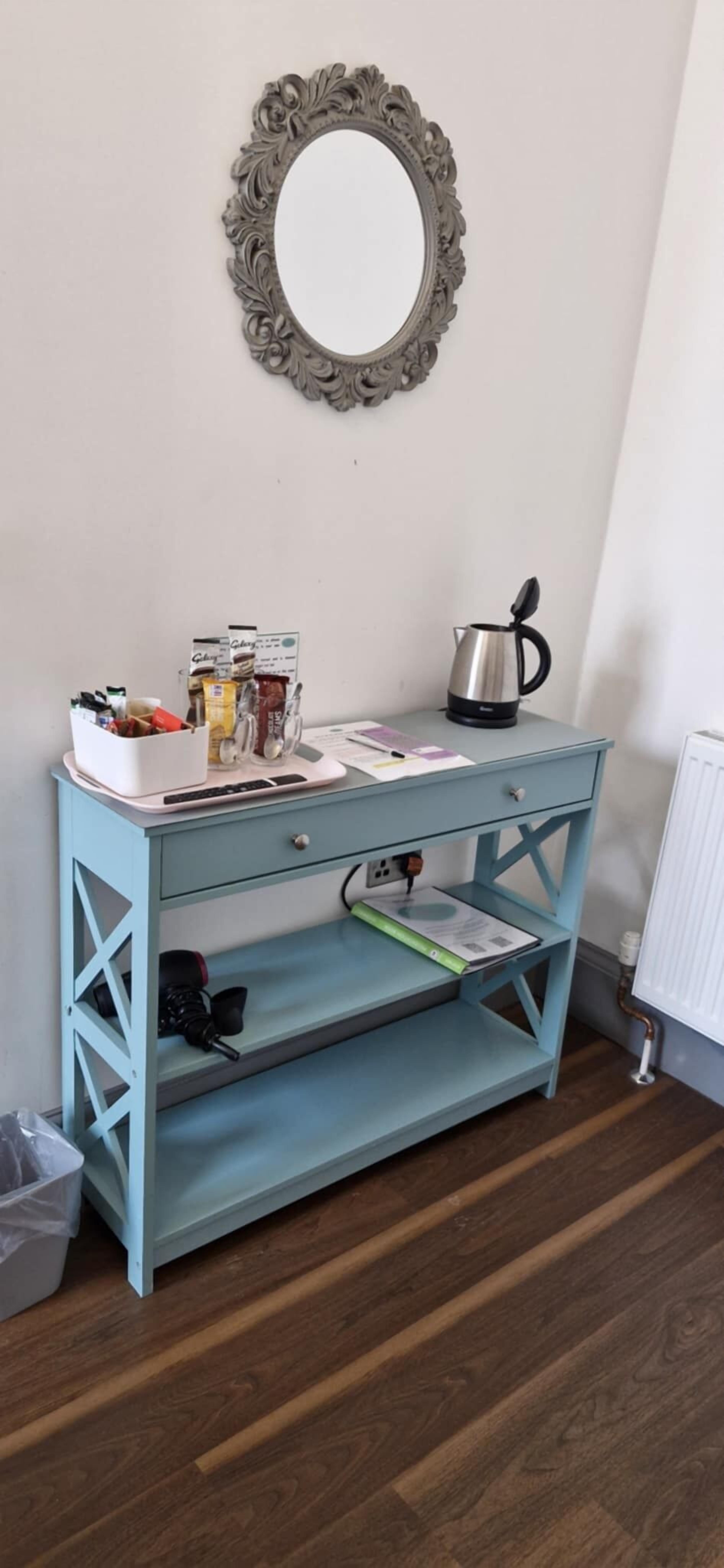 A light blue wooden desk with a kettle, a coffee maker, and various items on top.