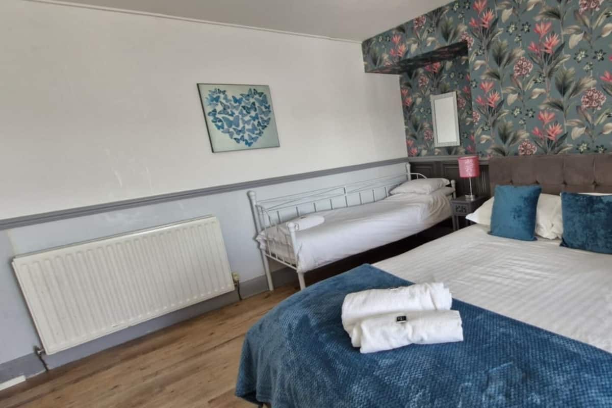 A bedroom with a bed, a radiator, a nightstand, a lamp, and a floral wallpaper.