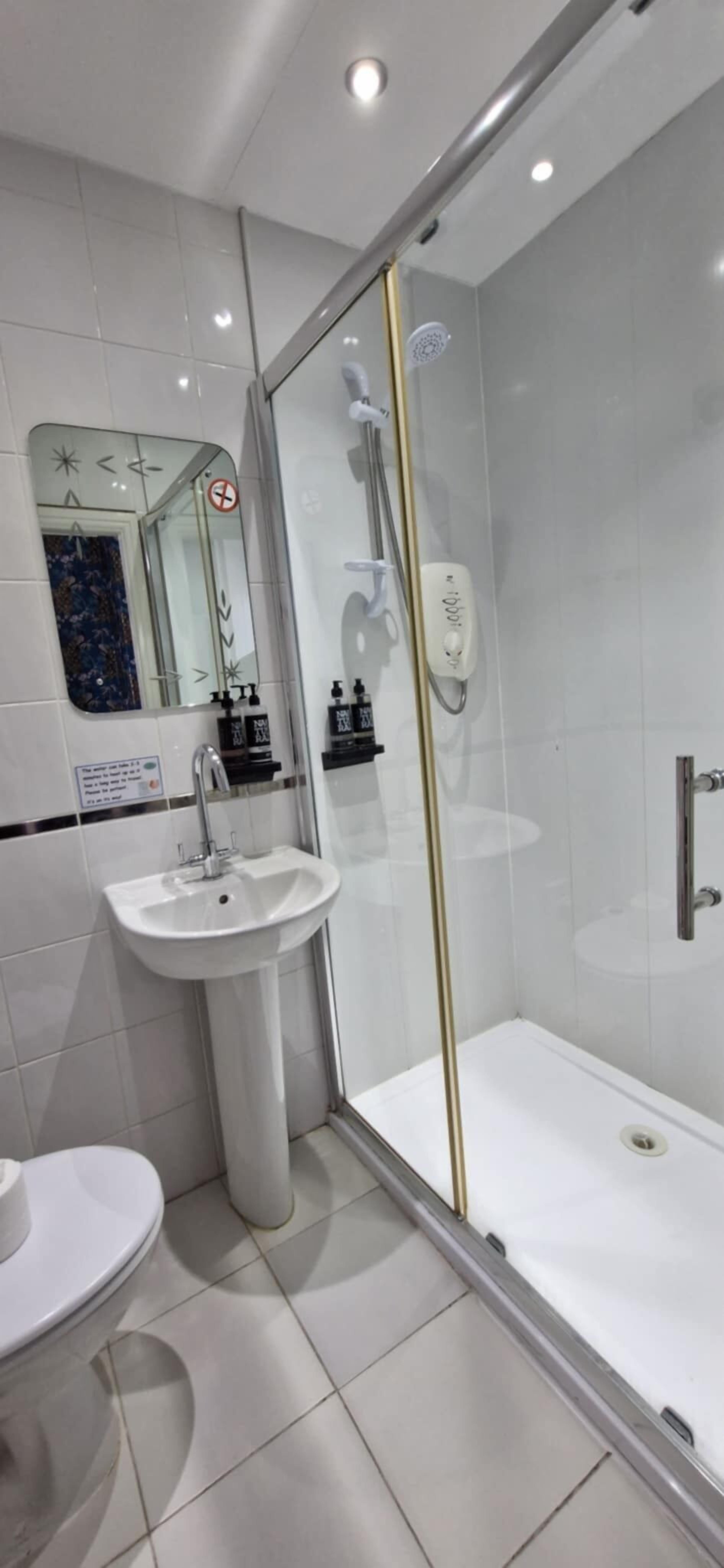 Un baño moderno con ducha de vidrio, lavamanos pedestal y retrete.